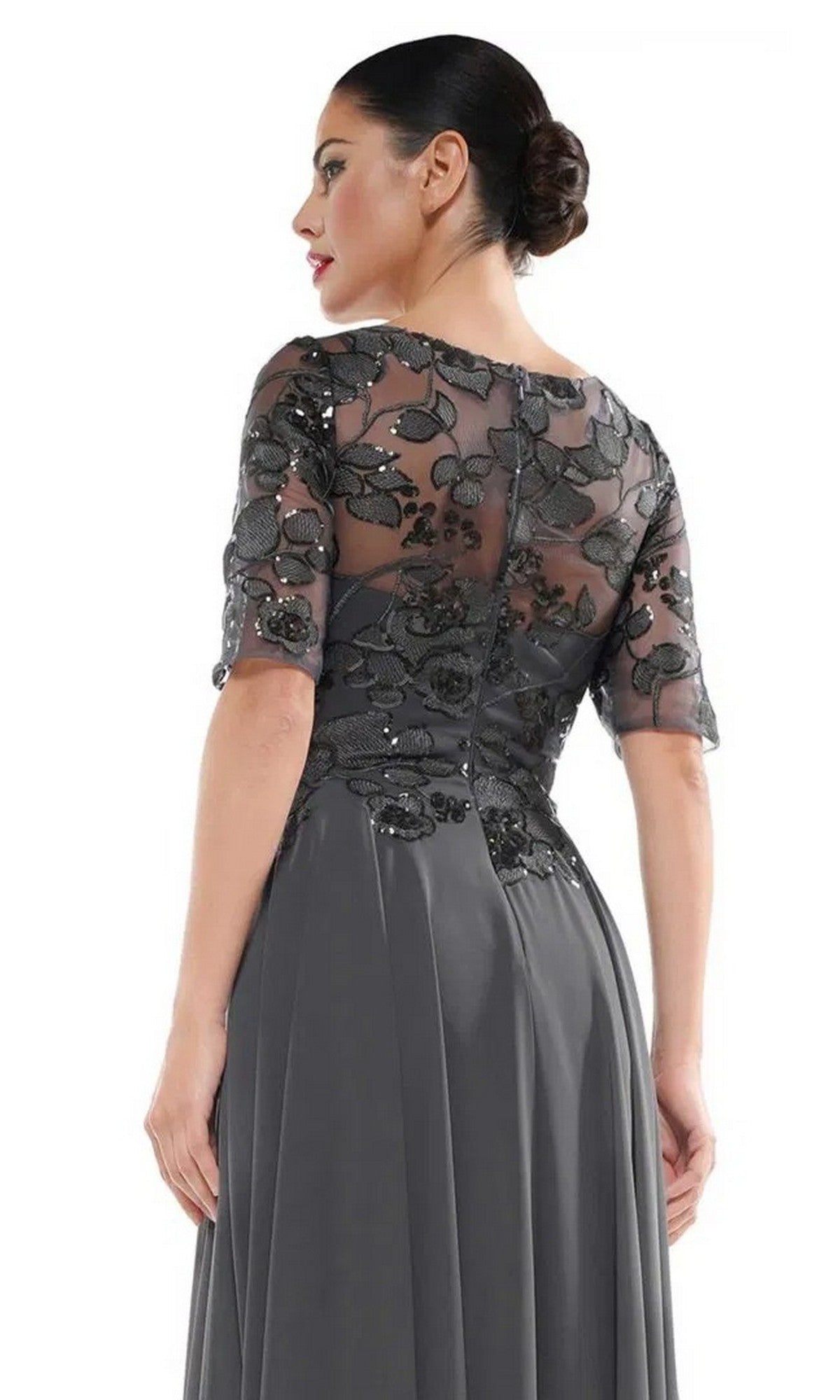 A woman in profile wears the Marsoni M286, a long grey formal dress with half sleeves and a sheer floral lace back.